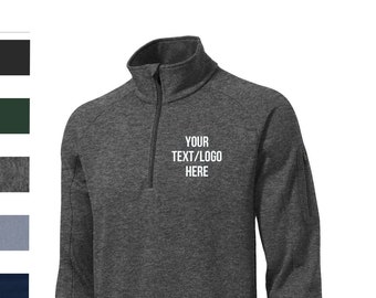 May include: A heather gray 1/4 zip pullover sweatshirt with a zippered pocket on the left side. The sweatshirt has a mock neck and the text "YOUR TEXT/LOGO HERE" is printed on the front.