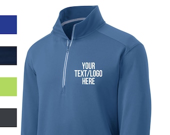 May include: A blue long-sleeve performance shirt with a quarter-zip closure. The shirt has a textured fabric and a white embroidered design that says "YOUR TEXT/LOGO HERE".