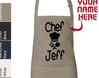 May include: A beige cotton apron with a black chef hat, crossed utensils, and the text "Chef Jeff" printed on the front. The text "YOUR NAME HERE" is also included on the apron.