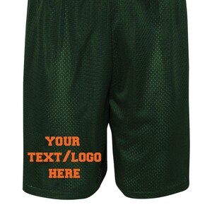 May include: Dark green athletic shorts with a mesh fabric. The shorts have a white tag on the waistband and orange text that says "YOUR TEXT/LOGO HERE".