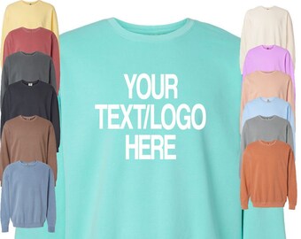 May include: A light turquoise sweatshirt with the text "YOUR TEXT/LOGO HERE" in white. The image shows a variety of crewneck sweatshirts in different colors, including yellow, red, gray, black, brown, and blue.