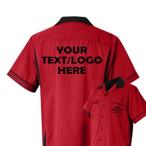 Puede incluir: Una camisa roja de manga corta con botones, cuello negro y ribetes negros en las mangas y los costados. La parte posterior presenta el texto YOUR TEXT/LOGO HERE en negro, y el &aacute;rea del bolsillo frontal muestra el texto YOUR TEXT/LOGO HERE.