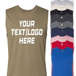 May include: A sleeveless t-shirt in olive green with the text "YOUR TEXT | LOGO HERE" in white. A stack of various colored sleeveless t-shirts are to the right, including white, gray, black, navy, pink, and red.