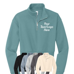 May include: A teal blue quarter-zip sweatshirt with a white embroidered design that says "Your Text/Logo Here".
