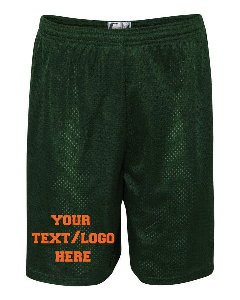 May include: Dark green athletic shorts with a mesh fabric. The shorts have a white tag on the waistband and orange text that says "YOUR TEXT/LOGO HERE".