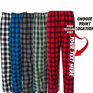 May include: Five pairs of pajama pants in various plaid patterns: black and white, blue, gray, green, and red. The red pair has the text "YOUR TEXT HERE" printed vertically and "YOUR TEXT/LOGO HERE" printed horizontally. The text "CHOOSE PRINT LOCATION" is also visible.