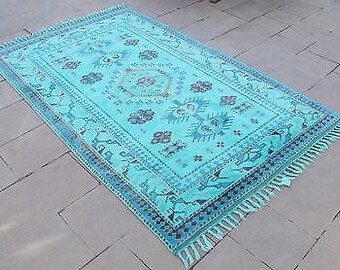 May include: A turquoise blue rug with a geometric pattern and fringe. The rug has a traditional design with a central medallion and repeating motifs.