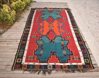 May include: A colorful rug with a geometric pattern in shades of red, orange, blue, and green. The rug has a black and white border with a repeating pattern. The rug is approximately 2.5 meters long.