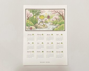 May include: A 2027 wall calendar featuring a rectangular illustration of a green frog wearing a patterned robe, sitting on a rock by a stream with cherry blossoms, bamboo, and a pagoda. Below the image are twelve monthly grids for the year 2027.
