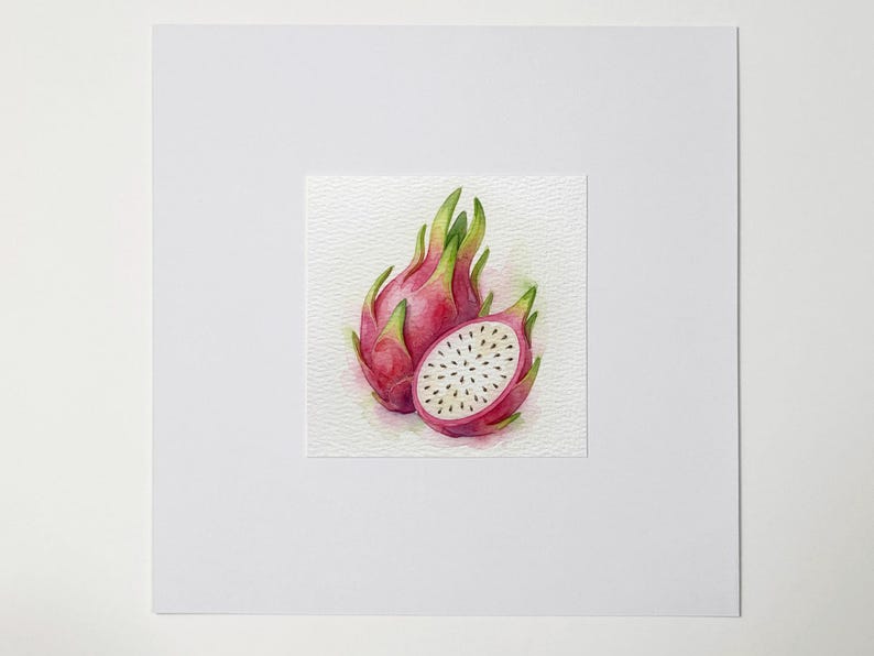 May include: Watercolor painting of two dragon fruits, one whole and one sliced open. The fruits are a vibrant pink with green accents and white flesh dotted with black seeds. The artwork is on textured paper.