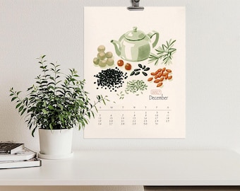 Peut inclure: Une page de calendrier mural pour décembre 2027 illustrée d'une théière vert clair, de brins d'herbes et de diverses graines et baies. La grille du calendrier affiche les jours du mois sous l'illustration sur un fond couleur crème.