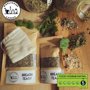 May include: An assortment of herbal teas and ingredients, including loose leaf tea in brown paper bags, a muslin tea bag, and fresh herbs. The bags have the text "BREATH TEASY" and the logo "WHOLESOME LARDER". A food hygiene rating of 5 is visible.
