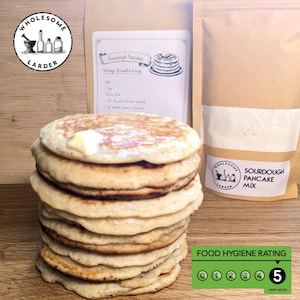 May include: A stack of golden-brown sourdough pancakes topped with butter. The image includes a bag of sourdough pancake mix and a recipe card. The food hygiene rating is 5, very good.