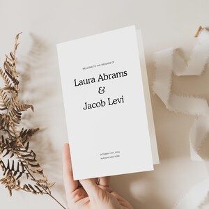 May include: A white wedding invitation card with black text. The text reads "Welcome to the wedding of Laura Abrams & Jacob Levi" and "October 12th, 2004 Hudson, New York".