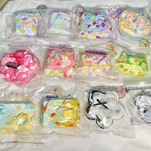 May include: A collection of 15 colorful, pastel-colored, and patterned keychains. The keychains are made of various materials, including fabric, plastic, and metal. The keychains are arranged in a grid pattern on a white surface. Some of the keychains feature cute designs, such as a butterfly, a flower, and a heart. The keychains are all different shapes and sizes.
