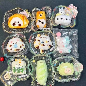 May include: Nine colorful, squishy toys in clear plastic packaging. The toys are shaped like animals and food items, including a bear, cat, and bread. Each toy has a unique design and color scheme, with details like facial features and patterns.
