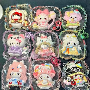 May include: Nine colorful, packaged figurines featuring cartoon characters with large eyes, bows, and decorative outfits. The figurines are in clear plastic packaging with decorative edges. The characters have various hairstyles and accessories, including balloons and small animal companions.