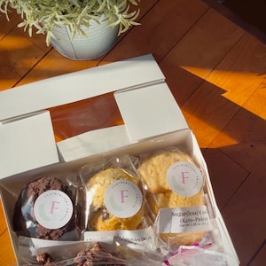 May include: A white gift box with a clear window, containing a variety of baked goods. The box includes chocolate chip cookies, sugar-free cookies, and chocolate covered pretzels. The box is labeled "Featherweight Sweets" and has a pink "F" logo.