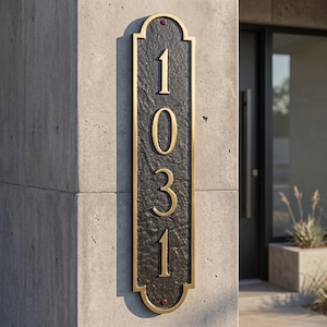 May include: A rectangular address plaque with the number "1031" in gold against a textured black background. The plaque has a gold border and is mounted on a concrete pillar. The numbers are large and easy to read.