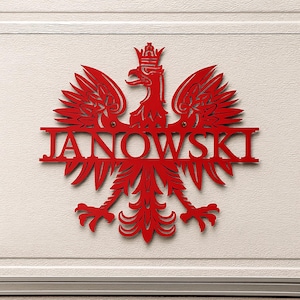 May include: A red metal wall sign featuring the Polish coat of arms, an eagle with a crown, and the name "JANOWSKI" in bold letters. The sign is mounted on a white surface.