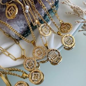 May include: A collection of gold-toned necklaces featuring circular pendants with embedded clear crystals forming various zodiac symbols. The pendants are attached to different styles of gold-toned chains, including curb, rope, and link chains, with some designs accented by small white faux pearls.