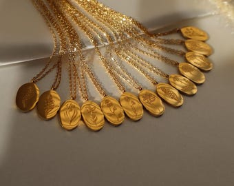 May include: A collection of gold-toned necklaces featuring oval-shaped pendants. Each pendant displays a unique, delicate floral engraving on its surface. The necklaces are arranged in a fan-like pattern, showcasing the metallic finish and chains.