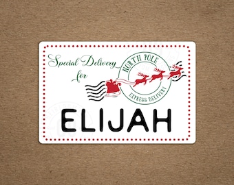May include: A white rectangular label with red dotted borders and the name "ELIJAH" in bold black letters. The label features the text "Special Delivery for" in green script, and a circular graphic with reindeer and the words "North Pole Express Delivery."