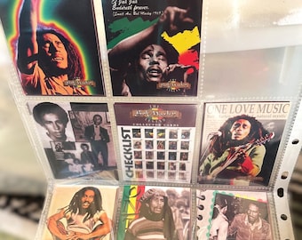 May include: A collection of Bob Marley trading cards in a clear plastic binder. The cards feature images of Bob Marley, song lyrics, and the words "ONE LOVE MUSIC". The cards are in various colors, including red, yellow, and green.
