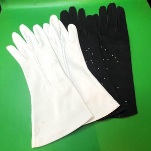 Peut inclure: Une collection de gants blancs et noirs. Les gants blancs sont lisses et classiques, tandis que les gants noirs présentent de petits ornements éparpillés. Les gants sont disposés sur une surface verte.