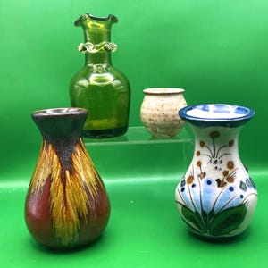 May include: Four decorative vases of varying shapes and sizes. One is green glass with a ruffled rim, another is a small, speckled ceramic pot, and a third is a white vase with blue floral designs. The fourth vase is brown, red, and yellow.