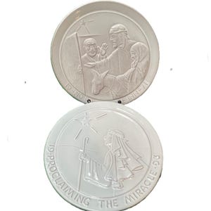 May include: Two white ceramic plates with embossed religious scenes. One plate shows a man at a door with text "19-NO ROOM INN-70". The other plate depicts a figure with a staff and text "19-PROCLAIMING THE MIRACLE-93".
