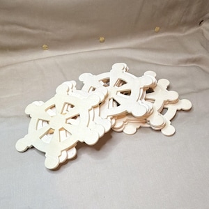 May include: A stack of multiple light-colored, unfinished wooden cutouts shaped like ship steering wheels. Each cutout features a central hub with eight spokes radiating outward to a circular rim with rounded handle protrusions along the edge.