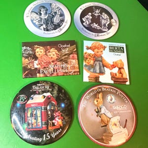 Puede incluir: Una colección de artículos decorativos de colección, que incluyen piezas redondas y rectangulares. Los artículos presentan imágenes de ángeles, niños y escenas navideñas. Algunas piezas tienen texto como "Artistry & Excellence".