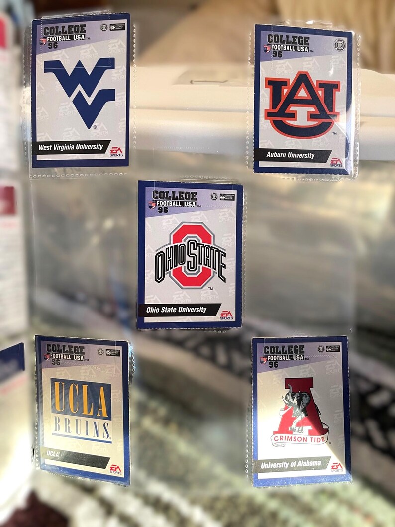 May include: A collection of College Football USA '96 trading cards featuring team logos and names. Cards include West Virginia University, Auburn University, Ohio State University, UCLA Bruins, and University of Alabama Crimson Tide.