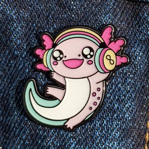 May include: A pink and white axolotl wearing headphones with a rainbow headband. The axolotl has large, black eyes and a pink smile. The headphones are turquoise and yellow.