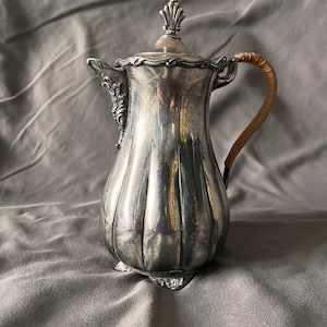 May include: A silver teapot with a fluted body and a decorative lid. The teapot has a brown wicker handle.