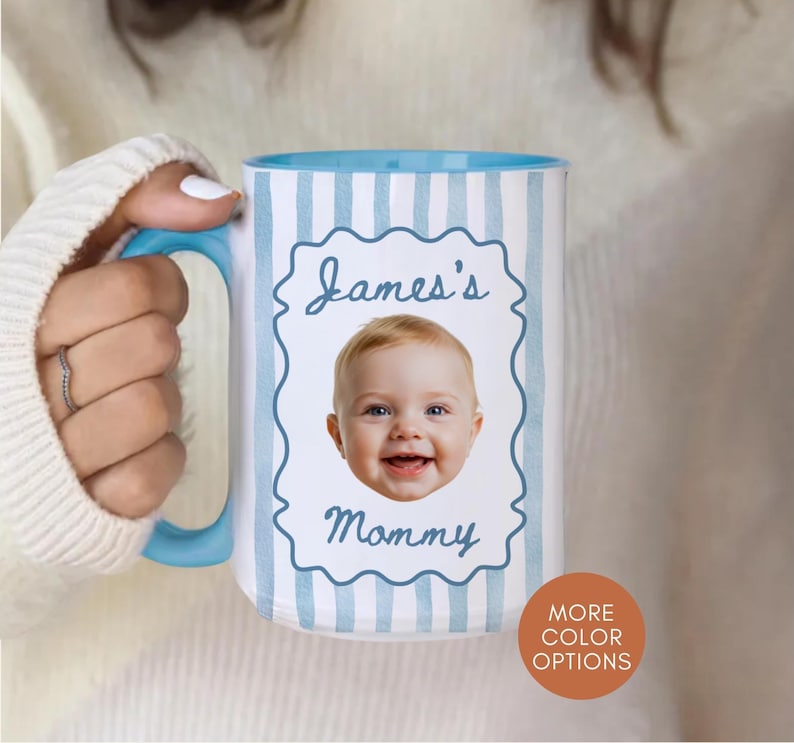 Op de afbeelding: Een grote witte mok met een lichtblauwe binnenkant en handvat. De mok heeft een foto van een baby met de tekst "James's Mommy" in een decoratief kader. De mok heeft verticale lichtblauwe strepen.