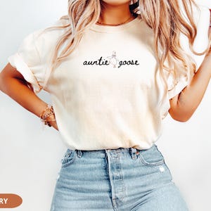 Puede incluir: Camiseta de color marfil con la frase "auntie goose" en escritura negra. El dise&ntilde;o incluye una sencilla ilustraci&oacute;n de un ganso. La camiseta se combina con vaqueros azules.