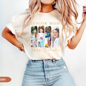 May include: Ivory-colored t-shirt with the text "SENIOR MOM 2026" in gold. The shirt features four framed photos of children. The name "Shaphie" is written in script below the photos. The shirt is made of soft material.