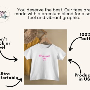 May include: White t-shirt with the word "threenager" in pink script and a pink bow. The shirt is hanging on a wooden hanger. Text on the image says "Won't Crack or Peel", "Ultra Comfortable", "100% US cotton", and "Produced in USA".