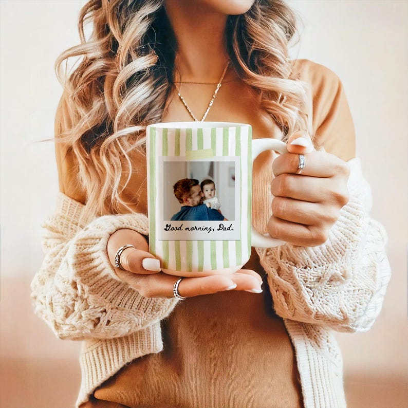 May include: White ceramic mug with vertical green stripes. A photo of a father and child is displayed on the front, with the text "Good morning, Dad." The mug has a large handle and is held by a person.