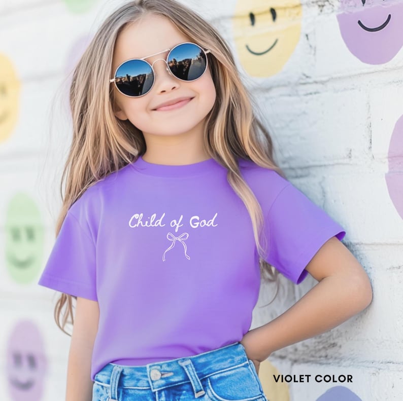 May include: A violet-colored t-shirt with the text "Child of God" and a bow graphic. The shirt is worn by a young person wearing sunglasses and blue jeans. The words "VIOLET COLOR" are at the bottom right.