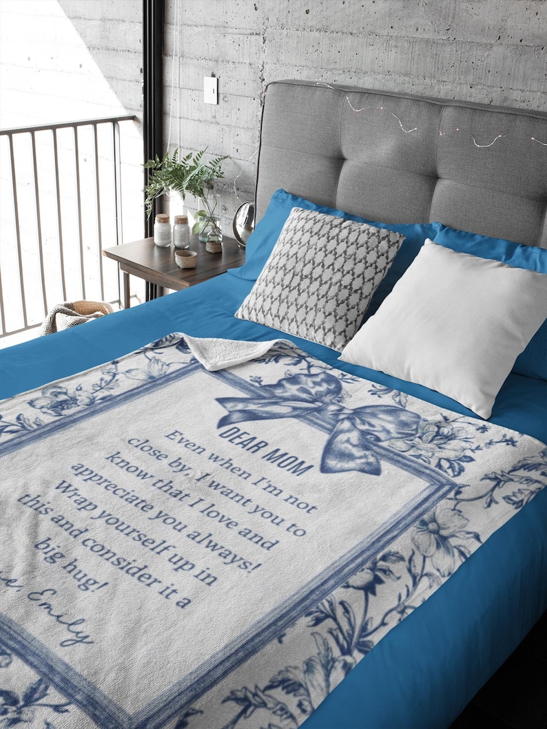Pode incluir: Cobertor branco e azul floral com o texto "DEAR MOM" e uma mensagem sincera. O cobertor apresenta uma borda decorativa e um design de la&ccedil;o, perfeito para um quarto aconchegante.