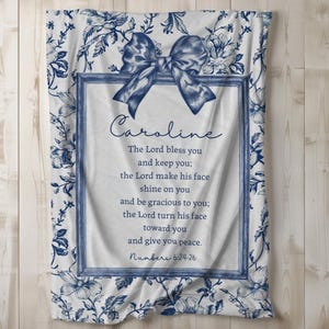May include: A white blanket with a blue floral pattern and a blue bow. The blanket has a framed section with the name "Caroline" and a Bible verse. The verse is from Numbers 6:24-26.