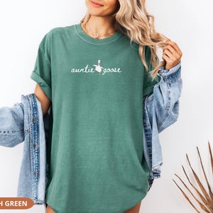 Puede incluir: Camiseta verde claro con la frase "auntie goose" en letra cursiva, acompa&ntilde;ada de una peque&ntilde;a ilustraci&oacute;n de un ganso. La camiseta es de color liso y tiene mangas cortas. El texto "LIGHT GREEN" est&aacute; en la parte inferior.