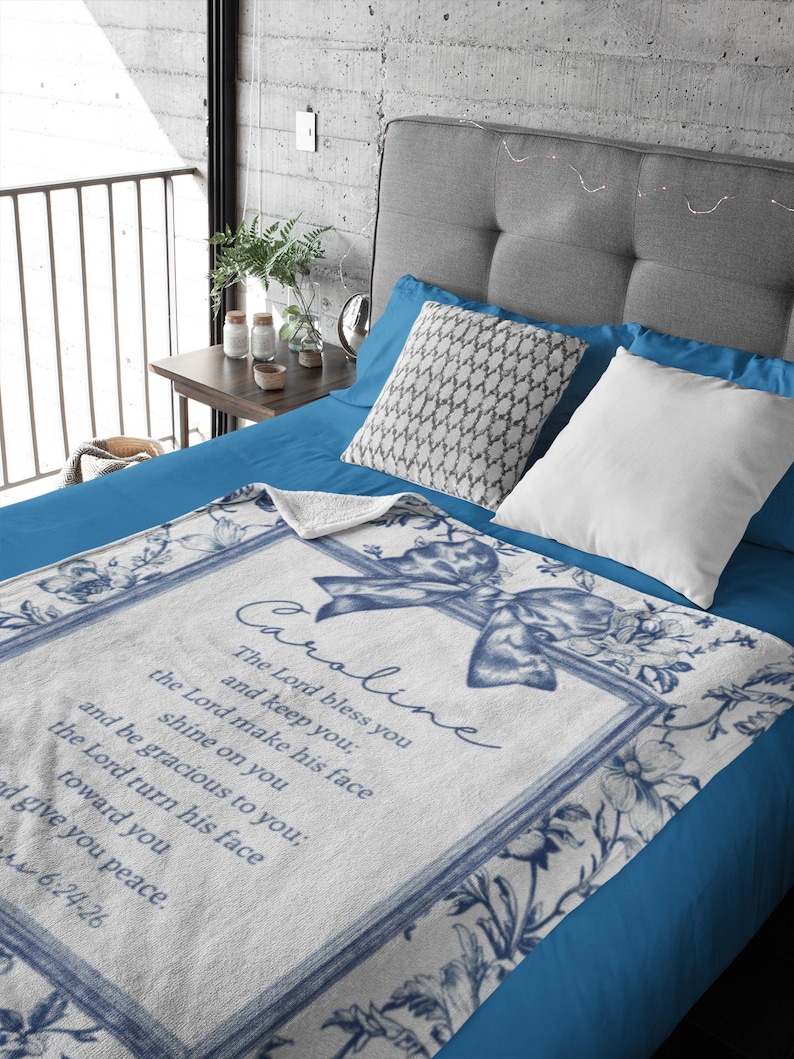 May include: White and blue floral throw blanket with the name "Caroline" and a Bible verse printed on it. The blanket has a blue border and a bow design. The blanket is on a blue bed.