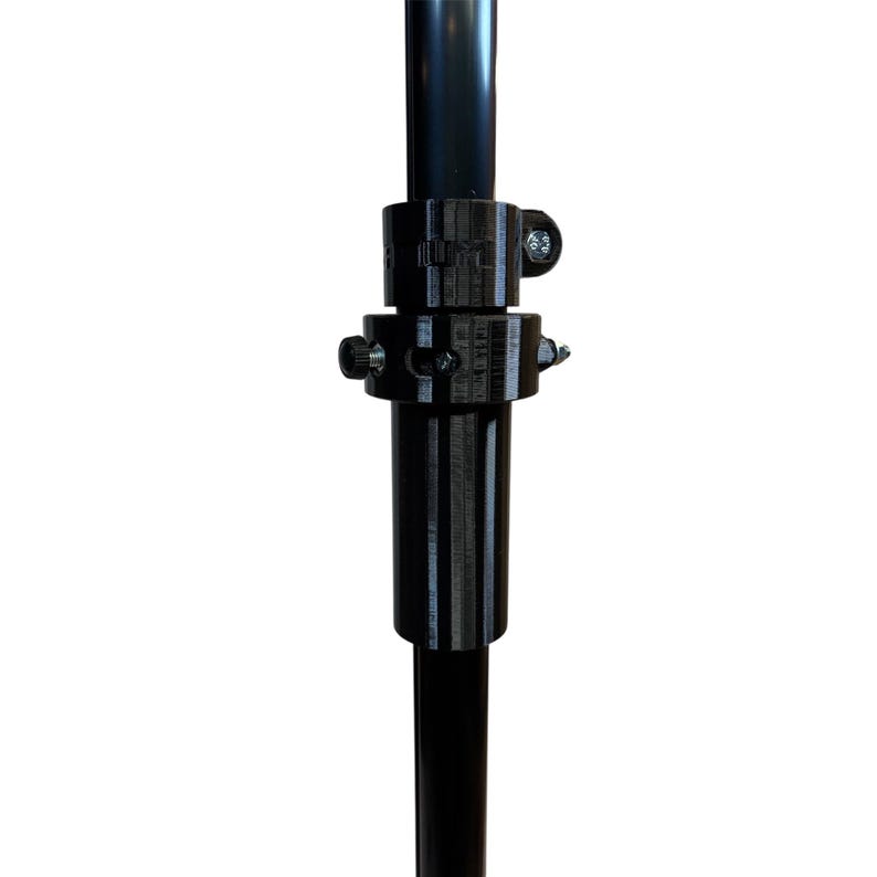 Pode incluir: Bra&ccedil;adeira ajust&aacute;vel de metal preto com parafusos, projetada para prender dois postes. A bra&ccedil;adeira &eacute; feita de um material dur&aacute;vel e possui uma s&eacute;rie de orif&iacute;cios e ranhuras para ajuste. O design permite um ajuste seguro e ajust&aacute;vel.