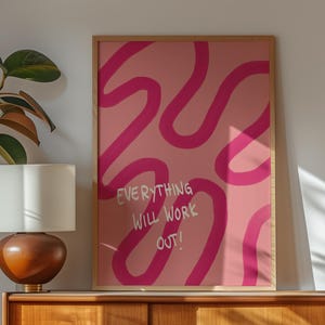 Könnte beinhalten: Ein rechteckiger Wandkunstdruck in einem hellen Holzrahmen mit einem rosafarbenen Hintergrund, dunkelrosa Wellenlinien und dem weißen Text "EVERYTHING WILL WORK OUT!", der mittig in vertikaler Ausrichtung aufgedruckt ist.
