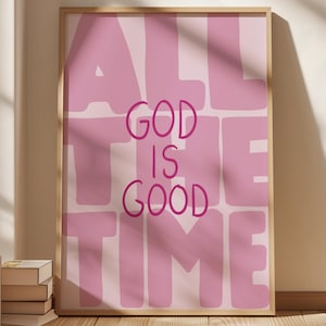 Könnte beinhalten: Ein rechteckiger Wandkunstdruck in einem hellen Holzrahmen mit dem Text ALL GOD IS GOOD THE TIME in dunkelrosa Schrift auf hellrosa Hintergrund, hinterlegt mit großen, blockartigen, unregelmäßigen Formen in einem helleren Rosaton.