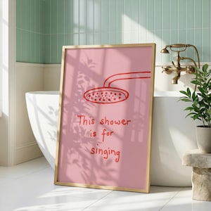 Könnte beinhalten: Ein rechteckiges gerahmtes Wandbild mit rosafarbenem Hintergrund, einer roten Strichzeichnung eines Duschkopfes und dem Text "This shower is for singing" in roter, handschriftlicher Schrift in der Mitte des Drucks.